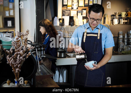 Ritratto del barista rendendo il latte per il cappuccino o il caffè nella caffetteria. cafe restaurant service, titolare di una piccola azienda, industria alimentare e delle bevande del concetto. Foto Stock