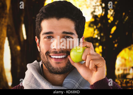 Close-up ritratto di uomo sorridente azienda apple contro caduta foglie in campo al park Foto Stock