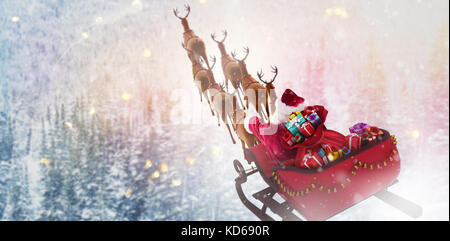 Angolo di alta vista di Santa Claus equitazione sulla slitta con la confezione regalo contro snowy pini su alp pendio di montagna Foto Stock