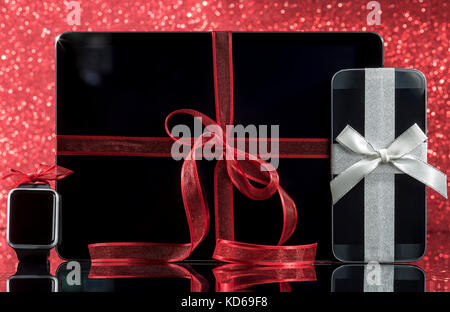 Smartphone e smartwatch e tablet pc e decorazioni per albero di Natale di vetro nero tabella su sfondo rosso. concentrarsi sullo smartphone. Foto Stock