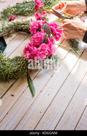 Fioraio al lavoro: creazione di una ghirlanda di legno con rami di pino e fiori di colore rosa e circondato dalle arti e mestieri. Foto Stock