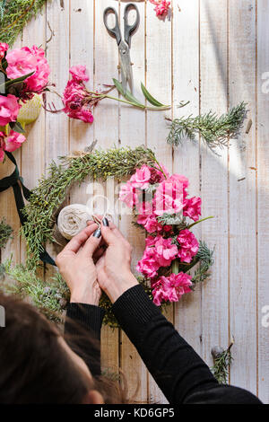 Fioraio al lavoro: creazione di una ghirlanda di legno con rami di pino e fiori di colore rosa e circondato dalle arti e mestieri. Avobe Foto Stock