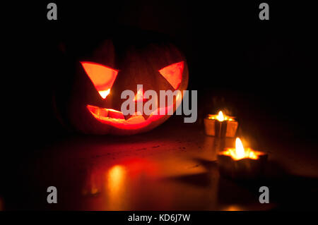 Scary Halloween zucca e melone jack-o-lanterne su sfondo nero illuminato con piccola rotonda e star candele. Il fuoco selettivo bokeh di fondo. Foto Stock