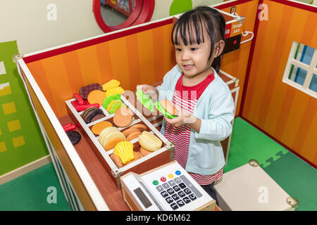 Cinese asiatici bambina role-playing a burger store al parco giochi al coperto Foto Stock