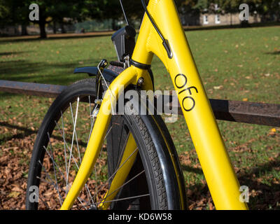 Un giallo OFO noleggiare biciclette o moto appoggiata contro una ringhiera in un parco a Cambridge Regno Unito Foto Stock