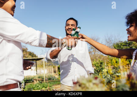 Giovani tintinnio di bottiglie di birra e sorridente durante il party in giardino del ristorante. Multi-etnico millennial avente birre al party all'aperto. Foto Stock