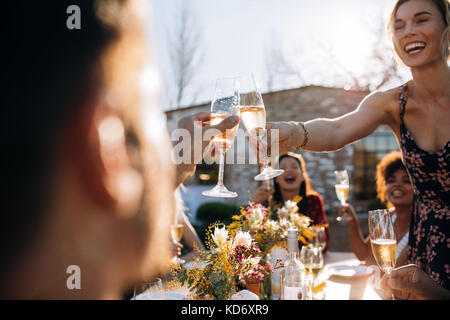 Sorridente giovane donna champagne di tostatura con un amico durante una festa all'aperto. I giovani godono a parte con focus sui bicchieri da champagne. Foto Stock