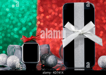 Smartphone e smartwatch e decorazioni per alberi di Natale nero sul tavolo di vetro sopra il verde e il rosso sfondo. concentrarsi sullo smartphone. Foto Stock