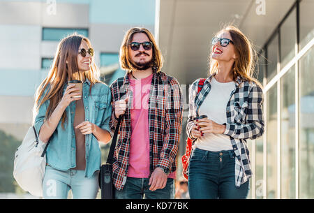 Gruppo di amici dello studente a piedi con tazze di caffè avente piacevole parlare, tramonto Foto Stock