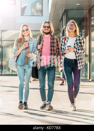 Gruppo di amici dello studente a piedi con tazze di caffè avente piacevole parlare, tramonto Foto Stock