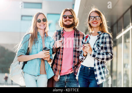 Gruppo di amici dello studente a piedi con tazze di caffè avente piacevole parlare, tramonto Foto Stock