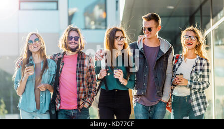 Gruppo di amici dello studente a piedi con tazze di caffè avente piacevole parlare, tramonto Foto Stock