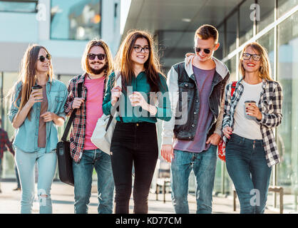 Gruppo di amici dello studente a piedi con tazze di caffè avente piacevole parlare, tramonto Foto Stock