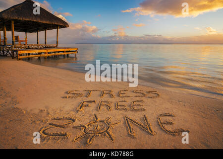 Primo piano scritto nella sabbia "stress free zone' al tramonto in isola Maurizio con pontile sul lato sinistro. Foto Stock