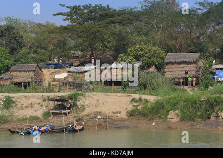 Un piccolo camion che trasportano pali di legno che passa attraverso un villaggio sul fiume Irrawaddy in Myanmar (Birmania). una piattaforma sopraelevata si trova accanto al fiume. Foto Stock