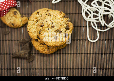 Biscotti natalizi, aggiungete pezzetti di cioccolato sulla tovaglia bambù rustico, nastro rosso e fiori Foto Stock