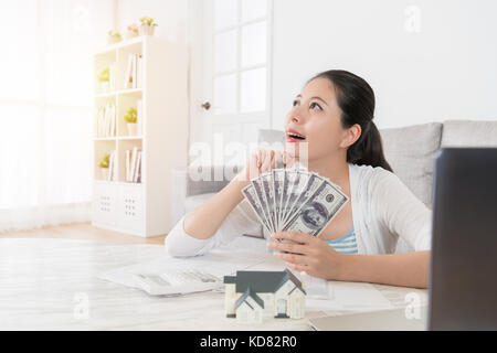 Felice giovane casalinga personali di conteggio di risparmio di denaro banconota in soggiorno e fantasticando pensando a come investire nuove station wagon Foto Stock