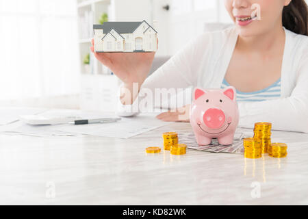Primo piano della bellezza donna giovane azienda piccola casa modello e conteggio conto moneta contante salvadanaio pianificazione acquisto nuova casa di famiglia con selective Foto Stock