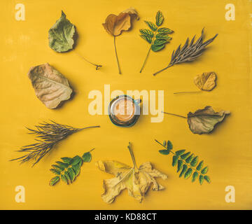 Caduta il concetto di caffè. Flat-lay della tazzina circondato da essiccato giallo e verde foglie di albero su giallo senape di legno verniciato di sfondo, vista dall'alto Foto Stock