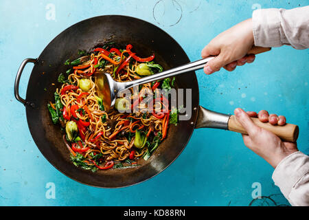 Udon STIR FRY Tagliatelle con funghi Oyster e verdure in padella wok e maschio di mani su sfondo blu Foto Stock