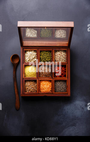 Superfoods e selezione dei cereali in scatola di legno: OAT, mung, quinoa, bulgur, semi di lino, goji berry, polba, lenticchia e chia su sfondo scuro Foto Stock