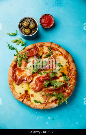 Pizza con mozzarella prosciutto e foglie di rucola su sfondo blu Foto Stock