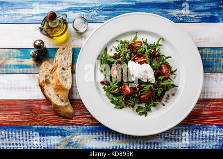 Con insalata di rucola, pomodori secchi, olio di semi di girasole e la ricotta sulla piastra bianca su sfondo di legno Foto Stock