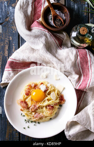 Tradizionale Italiana la pasta alla carbonara con tuorlo d'uovo, pancetta, parmigiano, timo, servita nella piastra bianca sul tessile su un vecchio ceppo di legno bac Foto Stock