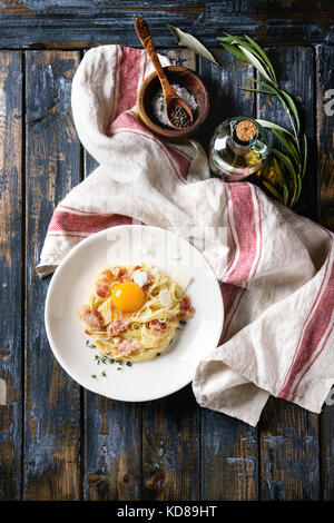 Tradizionale Italiana la pasta alla carbonara con tuorlo d'uovo, pancetta, parmigiano, timo, servita nella piastra bianca sul tessile su un vecchio ceppo di legno bac Foto Stock