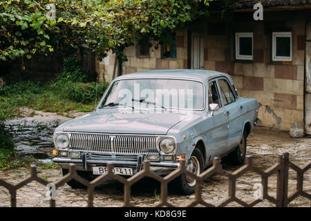 Parcheggiato Gray Volga GAZ-24, vecchia auto retrò vicino alla casa sotto la tettoia della vite verde. Foto Stock