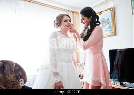 Bella damigella aiutando sposa a mettere su il suo matrimonio orecchini in camera. Foto Stock