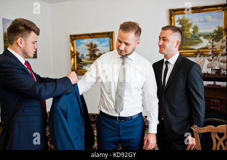 Groomsmen aiutare lo sposo a vestirsi per la sua cerimonia nuziale. Foto Stock