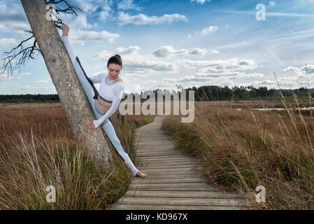 La donna a praticare yoga all'aria aperta in campagna facendo i gruppi contro un tronco di albero Foto Stock