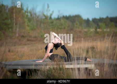 La donna a praticare yoga in campagna facendo una mezza prua, metà re cobra posa. Foto Stock