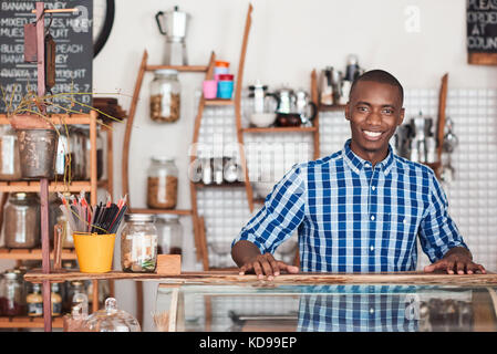 Sorridente imprenditore africani in piedi dietro il bancone del suo cafe Foto Stock