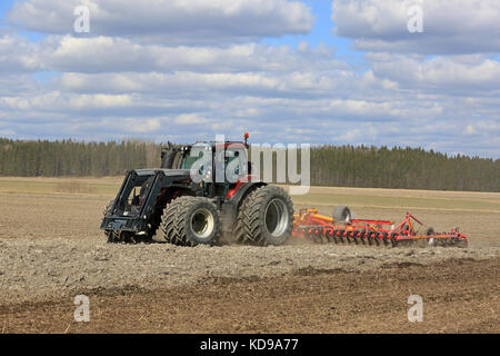 SALO, FINLANDIA - 7 MAGGIO 2017: Il trattore Red Valtra e il coltivatore a letto di semina Potila coltivano il campo in un bellissimo giorno di primavera. Foto Stock