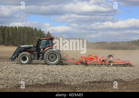 SALO, FINLANDIA - 7 MAGGIO 2017: L'agricoltore coltiva il campo con il trattore Valtra rosso e il coltivatore a letto di semina Potila in un bellissimo giorno di primavera. Foto Stock