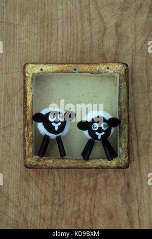 Due comici piccoli modelli di nero e di bianco pecora con gli occhi a bulbo in piedi nella piccola casella di oro Foto Stock