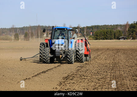 SALO, FINLANDIA - 14 MAGGIO 2017: L'agricoltore coltiva il campo con il trattore blu New Holland e la seminatrice in una giornata limpida di primavera nel sud della Finlandia. Foto Stock