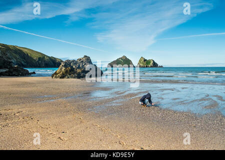 Una donna che esamina le conchiglie trovate sulla spiaggia di Holywell Bay. Gull Rocks a Holywell Bay, una delle location iconiche del film Poldark in Cornovaglia. Foto Stock