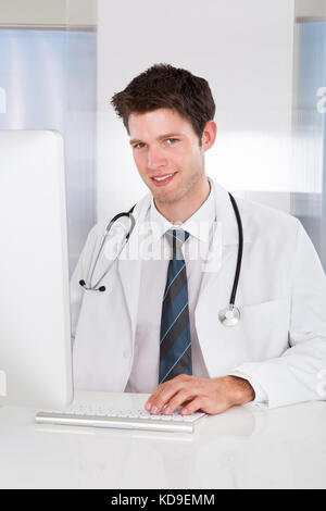 Ritratto di felice medico maschio utilizzando il computer al banco in clinica Foto Stock