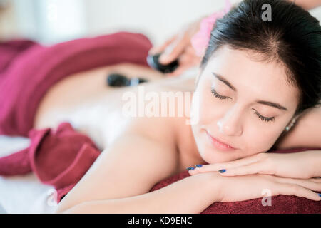 Bella giovane donna asiatica ricevendo la terapia rock massaggio nella spa salone. Mano Messa rock femminile sul retro, spa concept. Foto Stock