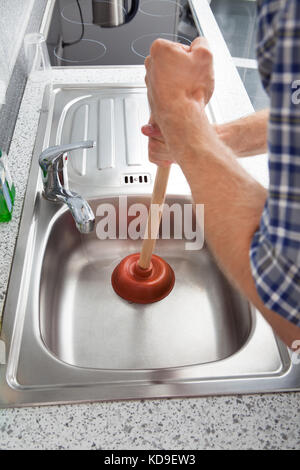 Primo piano dell'uomo utilizzando lo stantuffo nel lavello da cucina Foto Stock