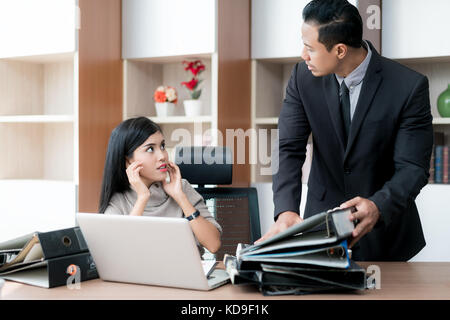 Rabbia imprenditore manager tenendo le cartelle sul suo subordinato tabella. imprenditrice sotto stress a causa di un eccessivo lavoro. Foto Stock