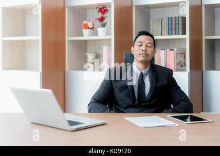 Stanco imprenditore oberato di lavoro dormendo su un computer portatile in un desk al lavoro nel suo ufficio. Asian businessman. Foto Stock