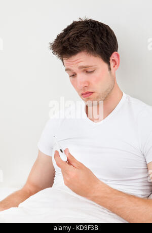 Giovane uomo che verifica la sua temperatura su un termometro digitale Foto Stock