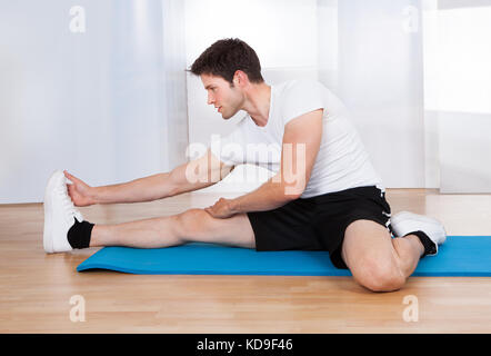 Giovane uomo felice in Sportswear facendo stretching su pavimento in legno duro Foto Stock