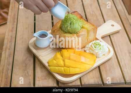 Pane tostato miele tè verde il gelato con maturi barracuda mango e panna montata nella piastra di legno su un tavolo di legno. Foto Stock
