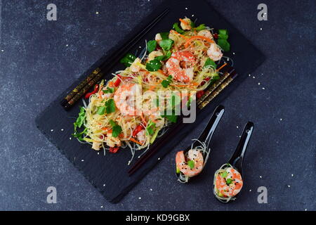 Tagliatelle con gamberi e le verdure su una pietra nera e piastra in zuppa tradizionale cucchiai su un grigio Sfondo astratto. cibo sano concetto Foto Stock