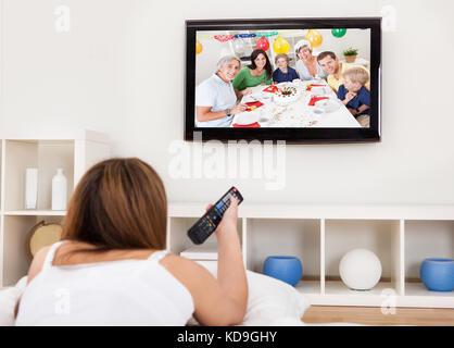 Giovane donna giaceva sul suo letto e guardare la televisione Foto Stock